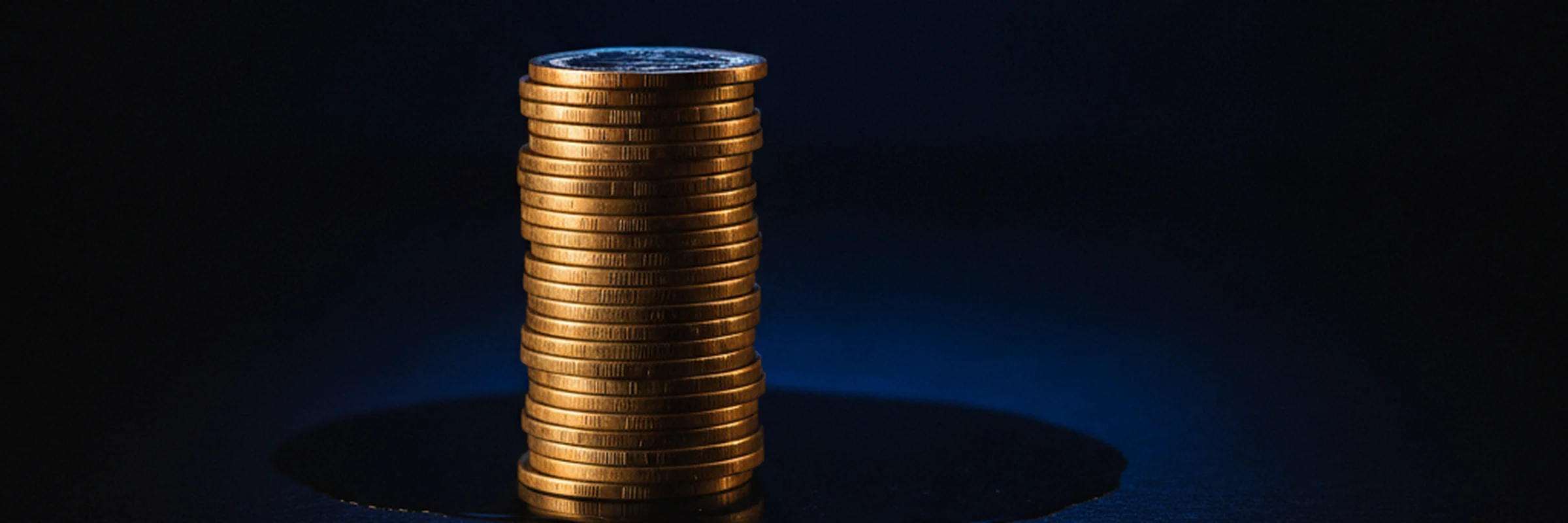 A stack of gold coins lit against deep royal-blue darkness